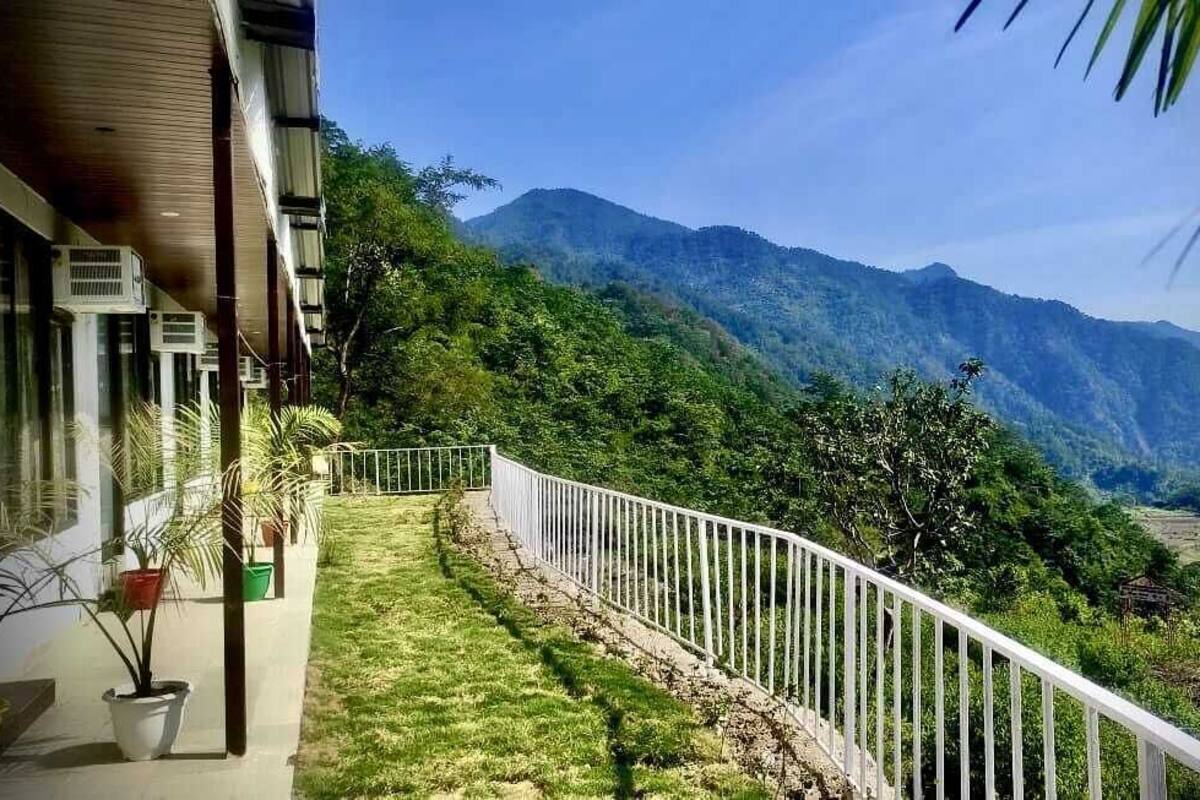 Un balcón con barandilla blanca que da a un paisaje verde exuberante y montañas.