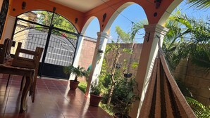 A covered patio with tiled flooring, a dining table with chairs, potted plants, and a hammock.
