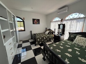 Quarto com duas camas, um guarda-roupa, um espelho e uma janela com detalhes em ferro.