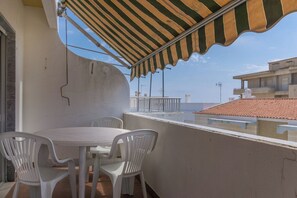 Uma varanda com mesa e cadeiras, um toldo listrado e vista para prédios.