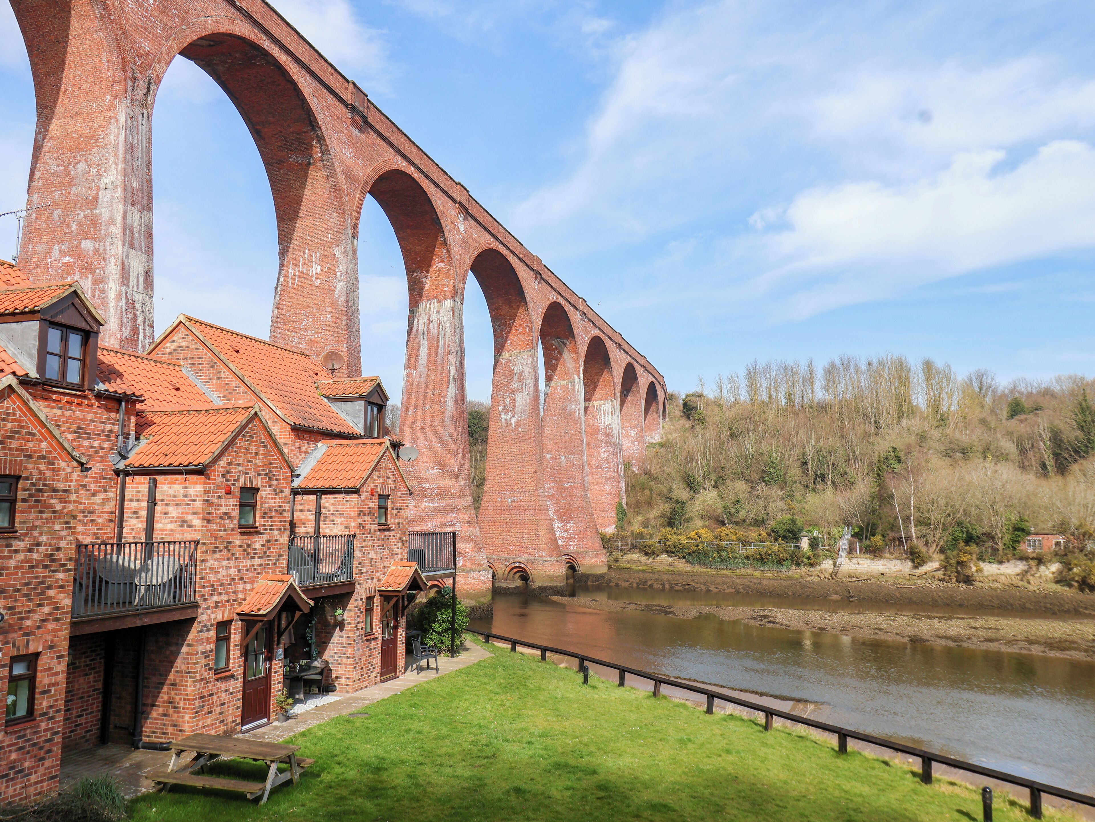 A brick building with a red-tiled roof and multiple arches, adjacent to a river.