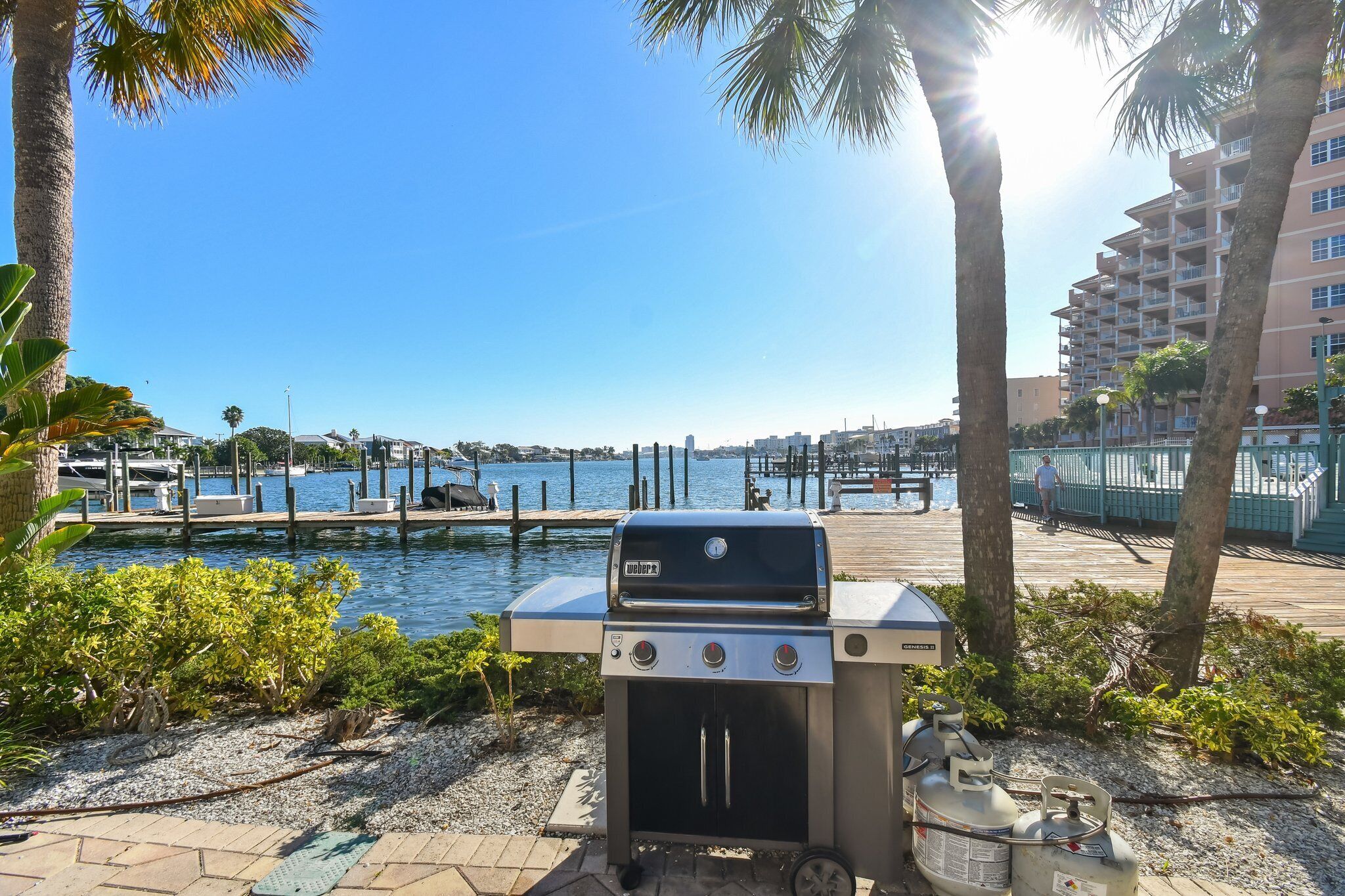A barbecue grill near a waterfront with a clear sky and palm trees.