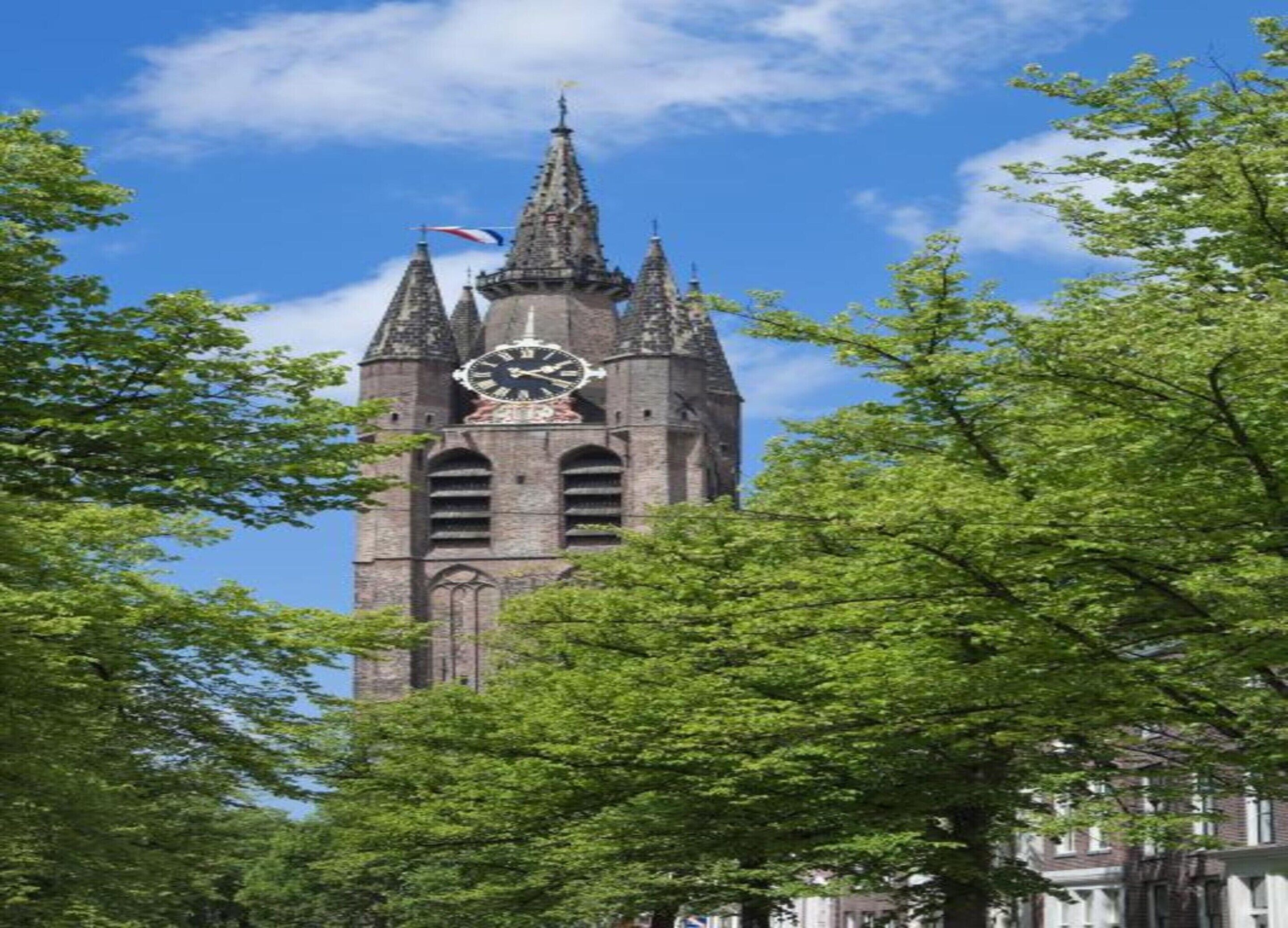 A historic clock tower with a clock face, surrounded by lush green trees.