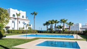 A pool area with two rectangular pools, surrounded by well-maintained grass and palm trees.
