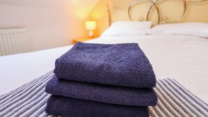 A neatly made bed with a folded dark blue towel in the foreground, a white pillow, and a striped blanket.