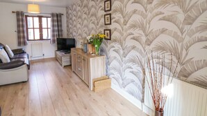 A living room with a wooden floor, a sofa, a TV, a cabinet, and a wall with a leaf pattern.