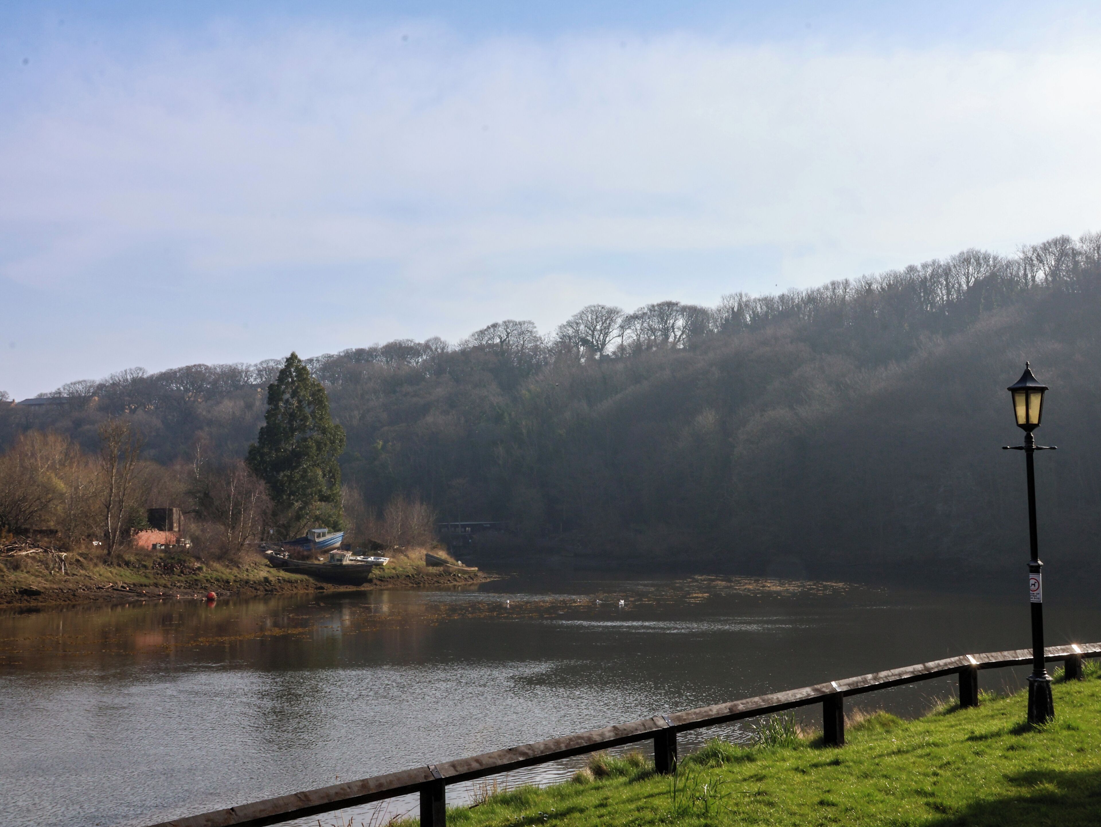 A calm lake with a wooden walkway and a lamp post.