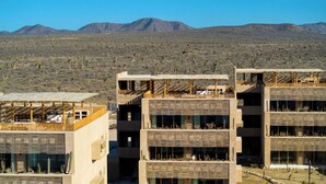 A modern building with multiple balconies, surrounded by a desert landscape with mountains in the background.