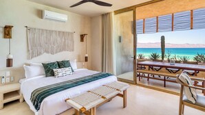 A bedroom with a bed, bedside table, bench, ceiling fan, and a view of the ocean through a sliding glass door. - Beachfront Vista Villa (La Ventana)