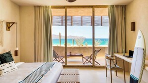 A bedroom with a bed, a desk, and a chair, a ceiling fan, and a view of the ocean.