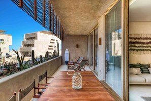 Ein Balkon mit Holztisch, Stühlen, einer Glastür und Blick auf Gebäude und Kakteen.
