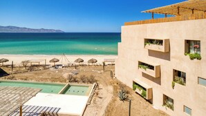 A modern building with balconies overlooking a beach and pool area. - Oceanview Vista Villa (La Ventana)