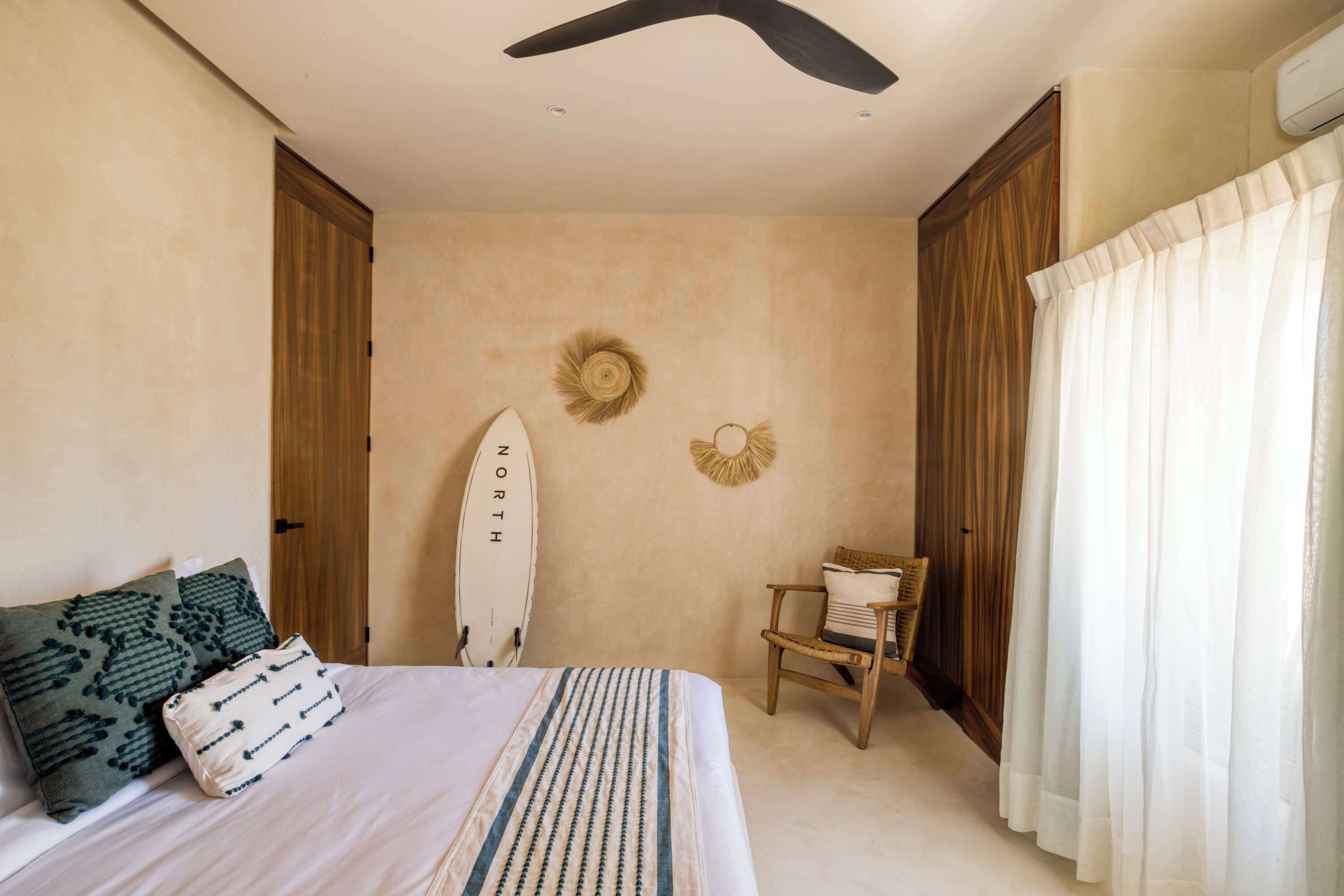 A bedroom with a bed, a surfboard, a chair, and a wall with a circular decoration.