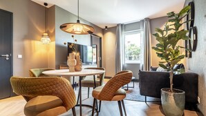 A modern living room with a dining area, featuring a round table, cushioned chairs, a large potted plant, and a sofa. - Stylish 2-bedroom Apartment in Delft (Delft)