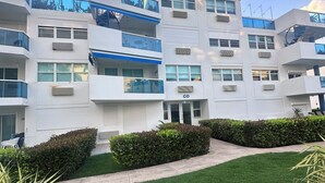 A multi-story building with balconies, air conditioning units, and a well-maintained lawn. - Cozy Studio in CostaMar Beach Village PR (Medianía Alta)