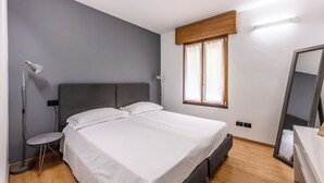 Ett modernt sovrum med en stor säng, sänglampor, ett litet runt bord och ett fönster med gardiner.