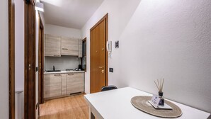 Ett kompakt kök med träskåp, en vit bänkskiva och ett litet matbord med en bordsduk och en vattenflaska.