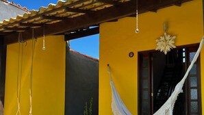 Ein gelbes Gebäude mit einer Veranda, einer Hängematte und einer Treppe zum Eingang.