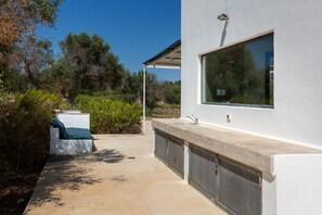 Un espacio exterior moderno con un banco de hormigón, un ventanal grande y una parrilla de metal.