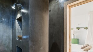 A modern bathroom with a large mirror, a shower with a handheld showerhead, and a small shelf with a basket.