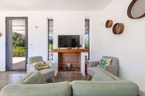 Un salon avec une cheminée, deux canapés, un téléviseur et une porte donnant sur un espace extérieur.