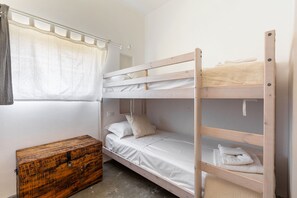 A bunk bed room with a wooden chest and a window with curtains.