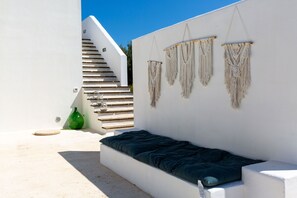 A white exterior wall with a built-in bench and macramé wall hangings.