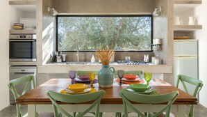 A modern kitchen with a dining area, featuring a large window, built-in appliances, and a view of trees.