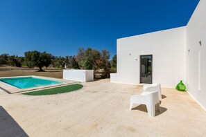 A modern outdoor area with a swimming pool, white walls, and a door leading to a covered patio.