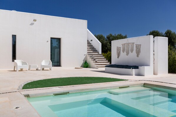A modern house with a pool, white exterior, and a staircase leading to a deck.