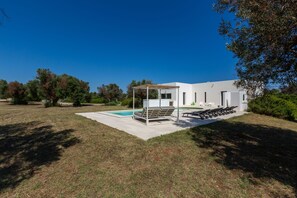 Ein modernes Haus mit Pool, Sitzgelegenheiten im Freien und einer überdachten Terrasse.