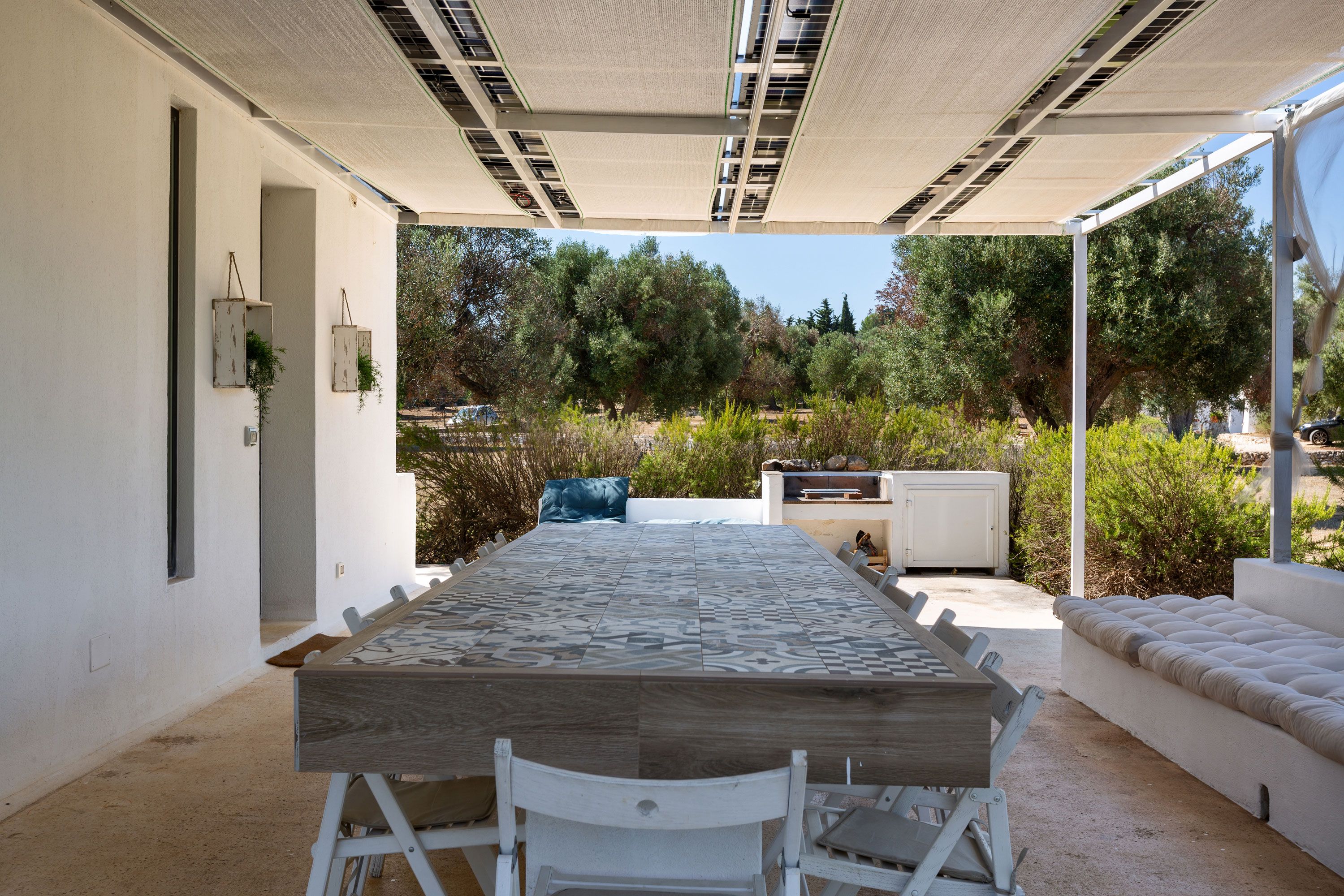 An outdoor patio with a long table and chairs, a built-in grill, and a covered seating area.