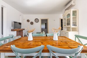 Comedor con una mesa de madera, sillas azul claro y dos jarras blancas con espigas de trigo.
