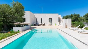 A modern pool area with a clear blue pool, white walls, and a minimalist outdoor seating area.