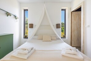 A bedroom with a canopy bed, two windows with views, a green cabinet, and a wooden door.