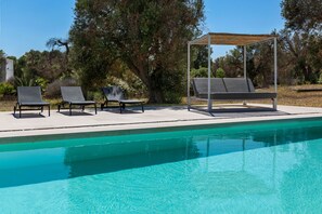 Una piscina con dos sillas de descanso y una zona de estar techada.