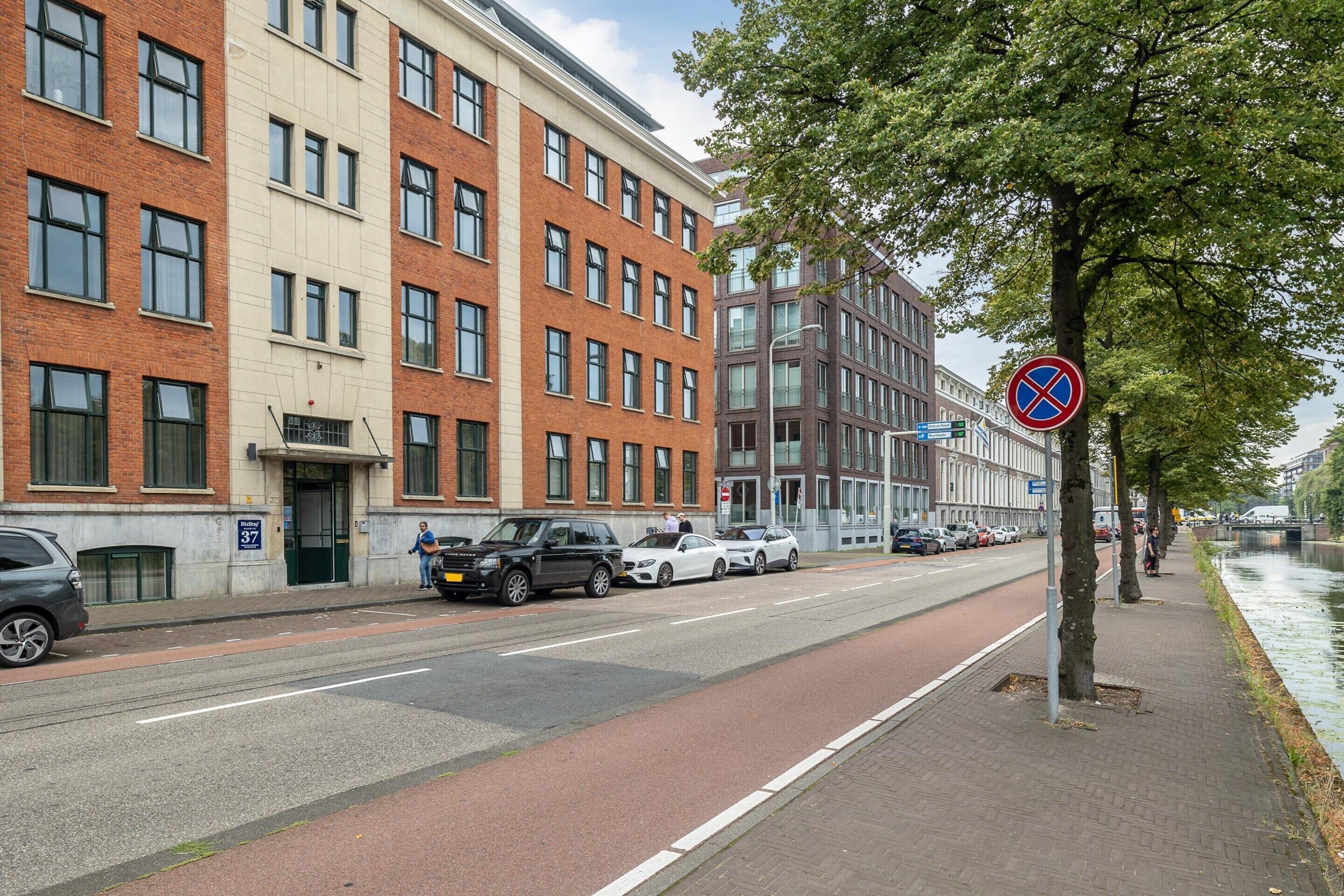 A street with parked cars, a no parking sign, and buildings with multiple windows.