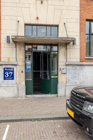 A building entrance with a green door, a sign for 'BizStay Maurits 37', and a black car parked in front. - Stylish Penthouse With 2 Bedrooms (The Hague)