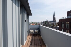 A balcony with a wooden floor and a black chair with patterned cushions. - Stylish Penthouse With 2 Bedrooms (The Hague)