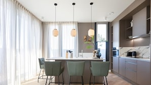 A modern kitchen with a central island, bar stools, pendant lighting, and a view of the outdoors. - Stylish Penthouse With 2 Bedrooms (The Hague)