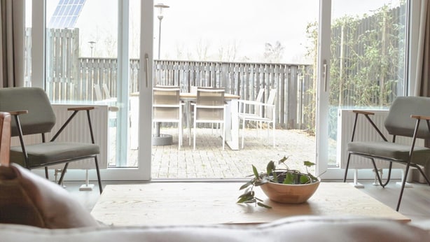 Et værelse med en stor skydedør, der fører til en udendørs terrasse. Terrassen har to stole og et bord.