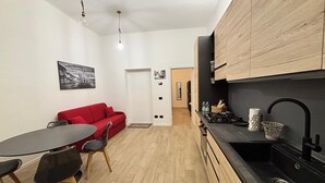 A compact kitchen with wooden cabinets, a black countertop, and a sink. There is a dining area with a red sofa and a table with chairs.