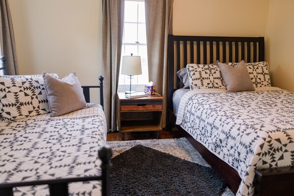 A bedroom with two beds, a nightstand, a lamp, and a window with curtains.