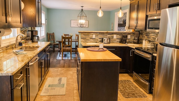 A modern kitchen with dark wood cabinets, stainless steel appliances, a central island, and a dining area with chairs and a table. - CF Ranch & Cattle Co. Guest House (Burbank)