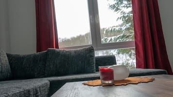 Un salon chaleureux avec un canapé gris foncé, une table basse en bois et un verre d’une boisson rouge.