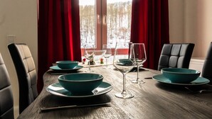 A dining table set with teal bowls and wine glasses, red curtains, and a view of a snowy landscape through a window. - Holiday Apartment With Lake View (Harzgerode)