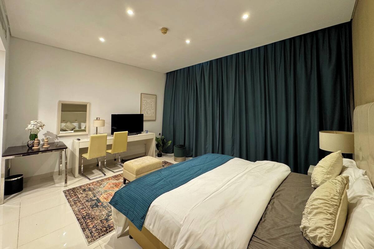 Una habitación de hotel con cama, escritorio, silla, televisión y un ventanal con cortinas.