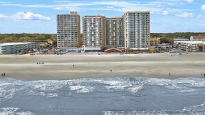 Een strand met hoge gebouwen op de achtergrond, een zandstrand en naderende golven.