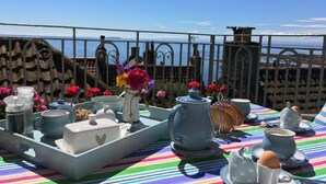 Une terrasse avec une table dressée pour le thé, agrémentée d’une variété de théières, de tasses et d’un plateau décoré de fleurs.