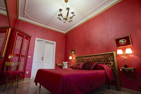 A red-walled bedroom with a large bed, a chandelier, and two bedside lamps. - VACATIONS IN THE HEART OF ROME COLOSSEUM (Roma)